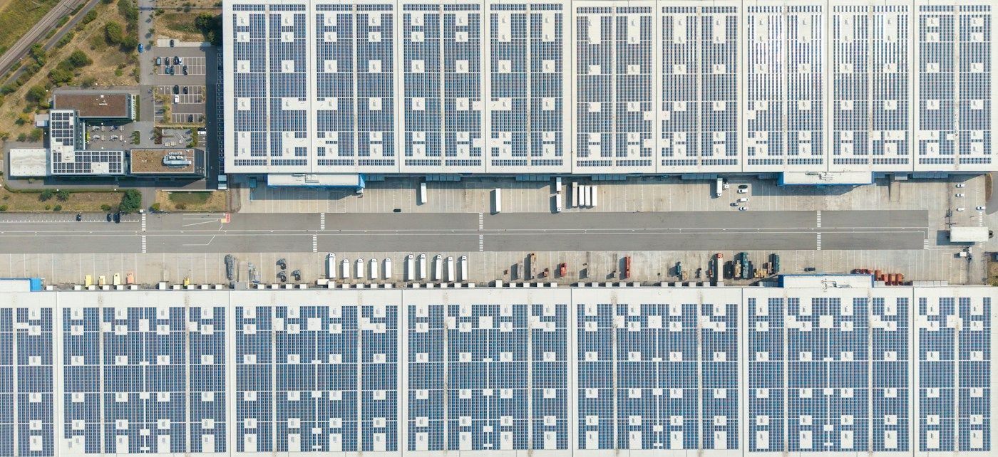 Large distribution warehouse roofs covered in rooftop solar panels, seen from the air